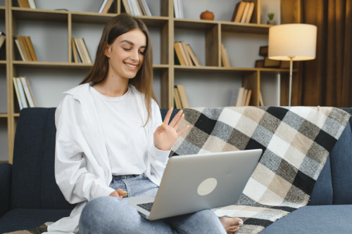 smiling attractive young woman sitting sofa using laptop communicating working online home happy teen girl typing computer enjoying writing blog chatting with friends social